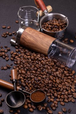 Kahve çekirdekleri, manuel öğütücü, kahve fincanı ve koyu arkaplanda duran kahve kepçeleri.