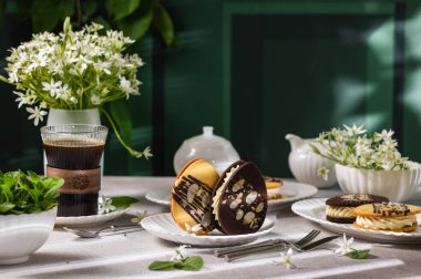 Çikolatalı sandviç kurabiyeleri ve bademle süslenmiş vanilyalı kahvaltı için zarif masada kahve ve bahar çiçekleriyle servis edilmiş.
