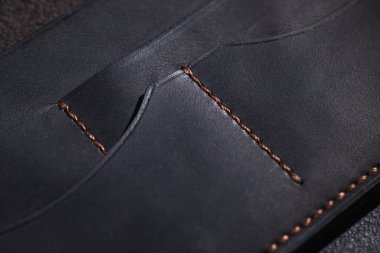 Bakır dikişleri ve çoklu cep bölmelerini vurgulayan siyah deri bir cüzdanın kapağı, yüksek kalitede işçiliği işaret ediyor.