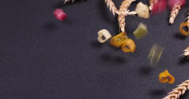 Çok renkli kalp şekilli makarna siyah bir arkaplan üzerine düşerek görsel olarak çekici bir düzenleme oluşturur.