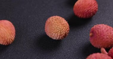 Olgun lychees koyu arkaplanda yuvarlanıyor, canlı kırmızı deri, taze doku, ve tropikal meyve doğal sulu görünüm