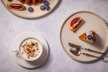 Bir fincan kapuçino, taze portakal dilimleri ve yaban mersiniyle lezzetli bir dilim pastanın tadını çıkarıyorum. Lezzetli bir kahvaltı veya atıştırmalık hazırlıyorum.