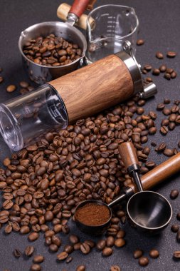 Koyu bir yüzeye saçılmış kavrulmuş kahve çekirdekleri, yanında bir el değirmeni, metal kepçesi ve bir ölçü öğütülmüş kahve ile aromatik bir tablo oluşturur.