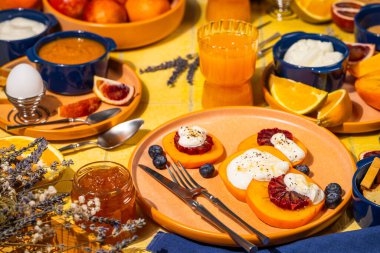 Canlı kahvaltı sahnesinde ricotta, kan portakalı ve bal ile birlikte taze meyve ve yoğurt dilimleri var.