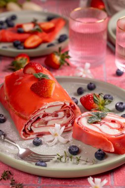 Pembe çilekli krep dilimleniyor ve taze çilek ve yaban mersiniyle servis ediliyor.