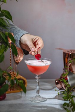 Barmen zarif bir bardakla canlı pembe bir kokteyl hazırlıyor taze bir kirazla, ferahlatıcı içeceğe son bir dokunuş ekliyor.