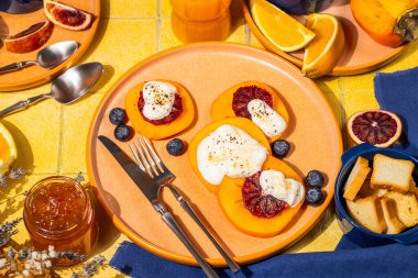 Portakal suyu, reçel ve melba tostla servis edilen canlı bir masada, ricotta peynirli, kanlı portakal dilimleri ve yabanmersinli lezzetli hurma tatlısı.