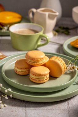 Yeşil tabakta portakallı makaronlar, arka planda kahve, mango ve süt sürahisi, lezzetli bir kahvaltı sahnesi hazırlıyorlar.