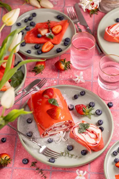 Lezzetli pembe çilekli kek tabakta yaban mersini ve bahar çiçekleriyle servis edilir ve canlı bir masa oluşturur.