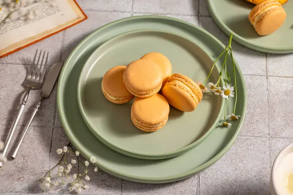 Canlı turuncu badem kurabiyeleri zarif yeşil tabaklar üzerinde güzel bir şekilde dizilmiş. Görsel olarak çekici bir sahne yaratıyor. Bu da harika bir aşçılık deneyimi olduğunu gösteriyor.