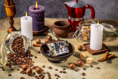 Mermer peynir, kahve çekirdekleri, macadamia fındıkları, yanan mumlar, tarçın çubukları, masada esmer şeker ve kahve demliği, samimi ve davetkar bir ortam yaratıyor.