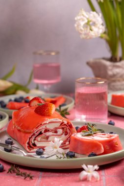 Pembe çilekli krep, yaban mersinli krep, krem peynirli ve taze çilekli, pembe masa üzerinde beyaz çiçeklerle süslenmiş.