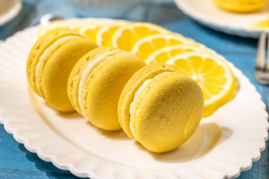 Canlı sarı limonlu badem kurabiyeleri taze limon dilimleriyle beyaz bir tabakta dizilmiş, cazip bir tatlı sunumu yaratıyor.