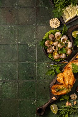 Sarımsaklı tereyağlı salyangoz, maydanoz ve kızarmış ekmek dilimleri yeşil kiremitli bir yüzey üzerinde servis edilir.