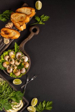 Sarımsaklı tereyağlı salyangoz, maydanoz, koyu arkaplanda kızarmış ekmek ve limon, lezzetli bir mutfak sahnesi yaratıyor.