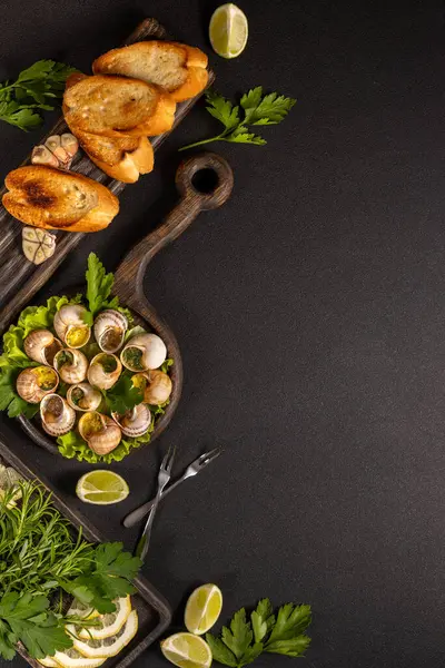 Sarımsaklı tereyağlı salyangoz, maydanoz, koyu arkaplanda kızarmış ekmek ve limon, lezzetli bir mutfak sahnesi yaratıyor.