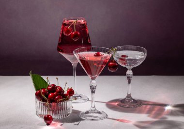 Kirazlı kokteyller ve bir kase taze kiraz içeren zarif cam eşyalar canlandırıcı ve canlandırıcı bir sahne yaratır.