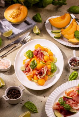Kavun ve prosciutto salatası taze fesleğen yaprakları, limon kamaları ve bir tutam tuz ve biberle süslenerek ferahlatıcı ve lezzetli bir yaz yemeği oluşturulur.