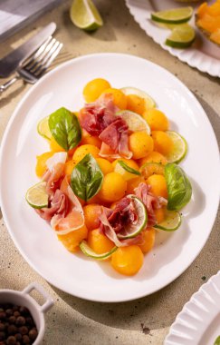 Küçük kavun topları prosciutto, kireç kamaları, taze fesleğen yaprakları ve taze yaz salatasında servis edilen karabiberle karıştırılır.