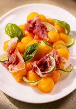 Limon ve taze fesleğen yapraklı kavun ve jambonlu salata, hafif bir yemek veya taze bir aperatif için canlı ve lezzetli bir seçenek sunar.