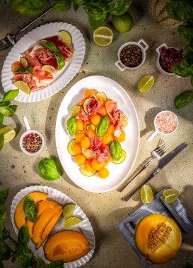 Kavun ve prosciutto aperatifi kireç ve fesleğen yaprakları ile servis edilir, beyaz tabaklar üzerinde güneş ışığıyla aydınlatılır, taze ve davetkar bir yaz yemeği oluşturur.