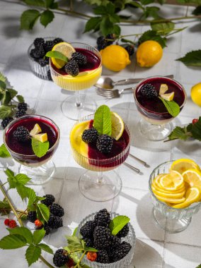 Canlı limon ve böğürtlen katmanlarıyla dolu, taze böğürtlen, limon dilimleri ve ferahlatıcı bir ikram için nane yapraklarıyla süslenmiş dört zarif tatlı fincanı.