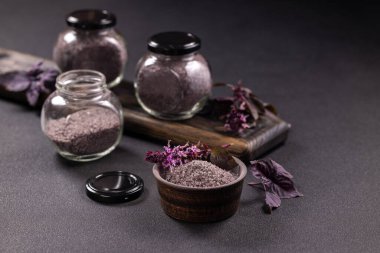 Cam kavanozlarda bulunan mor fesleğen ve küçük bir kase, koyu dokulu bir yüzey üzerinde sunulan aromalı ve aromalı mutfak yemeklerini geliştirir.