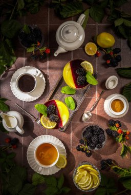 Böğürtlen ve limonlu panna cotta tatlısı, taze böğürtlen, limon dilimleri, nane şekeri, bir fincan çay ve sade kahve, çaydanlık ve sade sofra takımı.