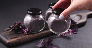 Dişi el, ahşap bir tahtaya küçük bir cam fesleğen kavanozu yerleştiriyor. Diğer kavanozların ve taze otların yanına. Lezzetli yemekleri tatlandırmaya hazır.