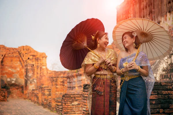 タイの古いタイの伝統的なスーツを着た2人のアジア人女性の幸せ顔と竹の傘 Unesco Thailandの世界遺産のアユタヤにある古い寺院に立って — ストック写真
