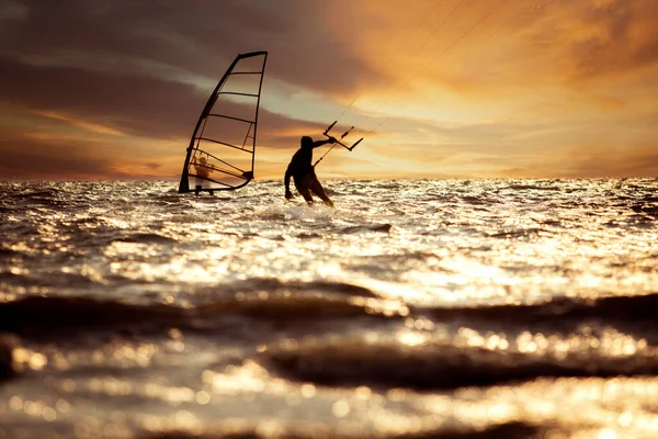 美しい夕日の空に対して急いで海面上でカイトサーフィンやウィンドサーフィンをしている男のシルエット写真 — ストック写真