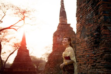 Tayland geleneği elbisesi giyen güzel Asyalı kadın Ayutthaya 'nın eski dünya mirası alanının tuğla duvarına karşı duruyor.