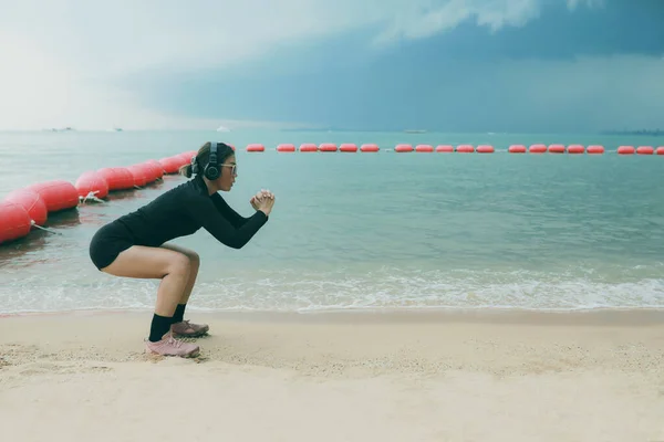 头戴耳机的女子在海滨进行蹲式运动 — 图库照片