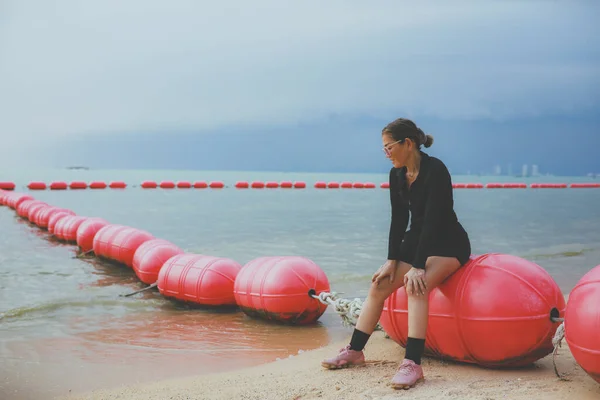 身穿黑色跑步运动服的妇女坐在海滩上的漂浮障碍物上 — 图库照片
