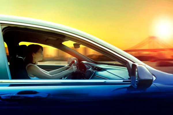 美しい夕日と街のスカイラインに向かって車を運転する女性 — ストック写真