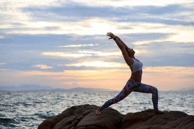 Deniz sahilinde yoga yapan bir kadın yükselen güzel güneşe karşı