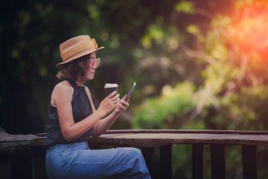 Güzel bir kadın akıllı telefondan mesaj okuyor ve elinde kahve fincanıyla terasta oturuyor.