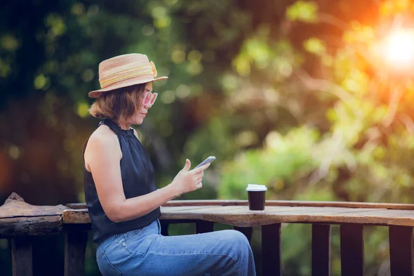 木製のテーブルの上にコーヒーカップとスマートフォンでメッセージを読んでいるかなりの女性 — ストック写真