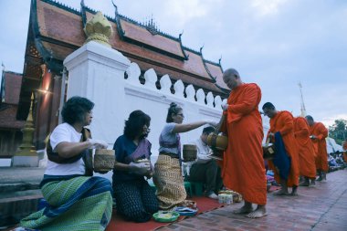 Luangprabang lao-july20,2023: Lao keşişi Luangprabang caddesindeki Asyalı kadından güzel wat sensoukharam tapınağı çitlerine karşı yapışkan pirinç ve yiyecek alıyor. 