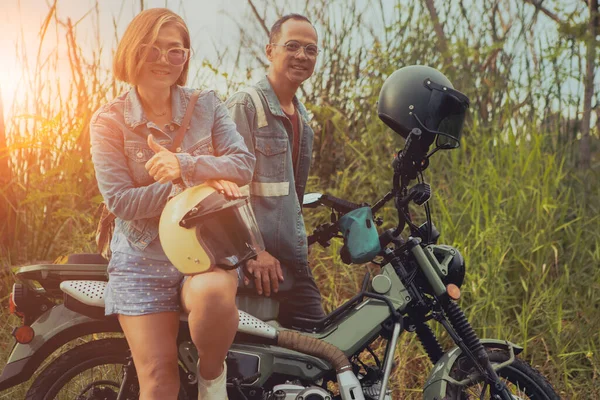 亚洲夫妇站在高绿草背景的内蒙古摩托车旁边 图库图片