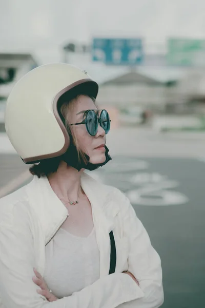亚洲妇女头戴防撞头盔站在城市道路旁边 图库照片