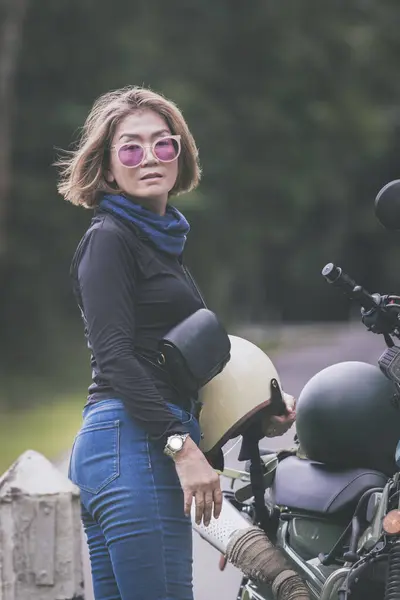 漂亮的女人 头戴安全帽 站在小型内胎摩托车旁边 免版税图库照片