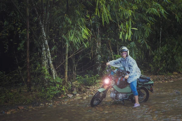 漂亮的女人骑着小摩托车穿过浅浅的小溪 图库图片