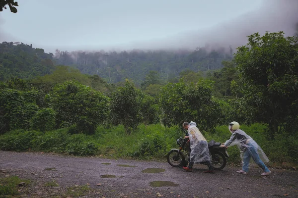 亚洲夫妇合作 在森林路中间推着一辆故障的摩托车 图库照片