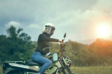 Güvenlik kaskı takan bir kadın arka planda küçük bir dayanıklı motosiklet sürüyor.