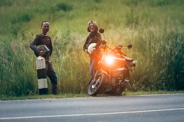亚洲夫妇头戴安全帽 站在漂亮的绿色草地上的小摩托车旁边 免版税图库照片
