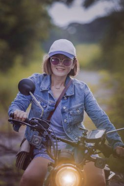 Güzel bir kadın toprak alanda spor dayanıklı motosiklet sürüyor.