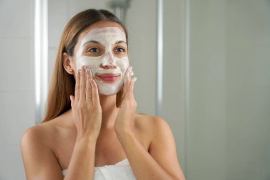 Yüzünde kilden bir maske olan güzel bir kadının portresi banyodaki aynada kendine bakıyor.