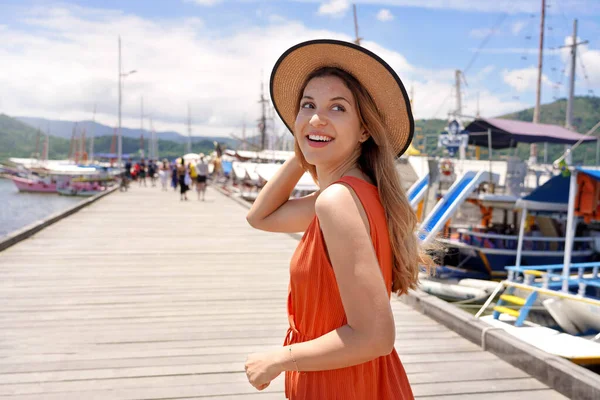 Portrait of smiling tourist woman walking on wooden pier where travel by ferry or rented boat or yacht to explore warm tropical destinations