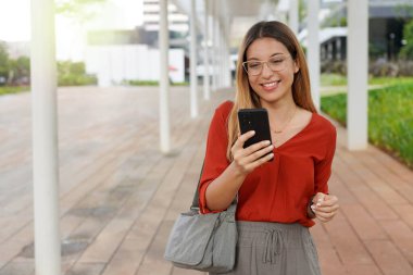 Brezilyalı üniversite öğrencisi dışarıda akıllı telefonunu izliyor.
